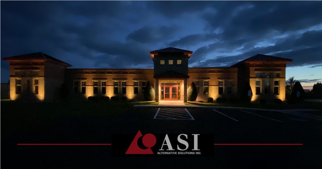 Our current office building at w3131 County Rd C, in Sheboygan Falls, WI. In this photo, the building is lit up in the night by lights shining up at each window and entrance.